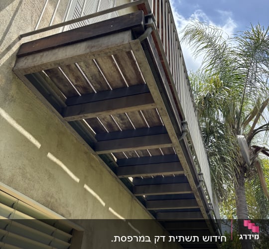 מרפסת עץ עם מעקה מתכת ליד עץ דקל